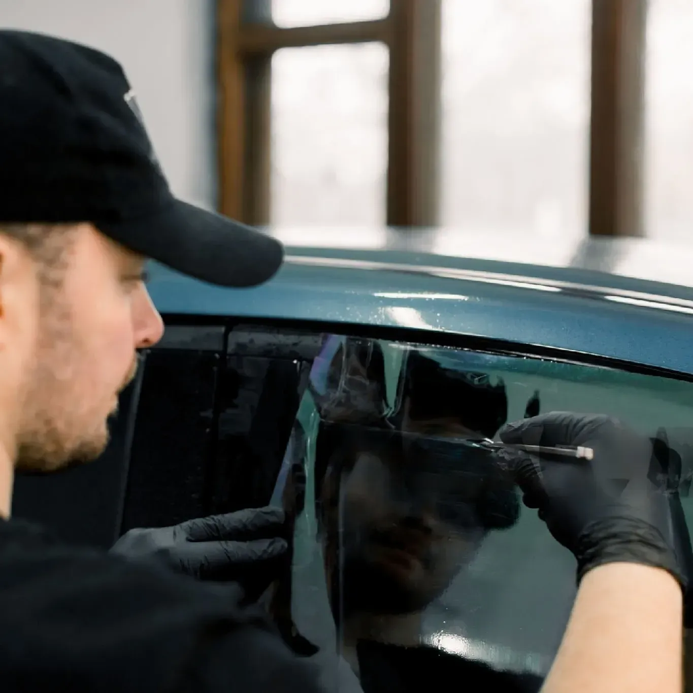 un hombre con sombrero y guantes está aplicando vidrios polarizados a la ventana de un auto.