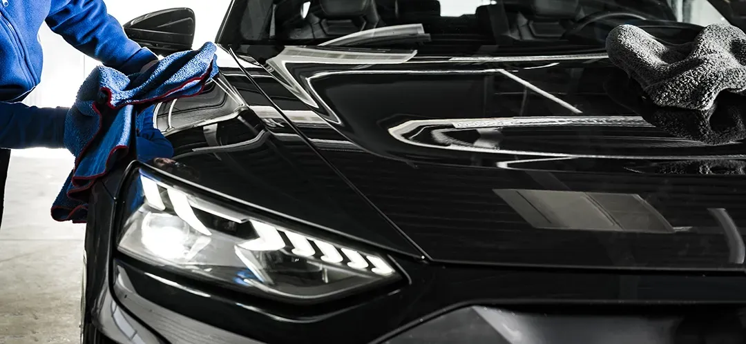 A man is cleaning a black car with a cloth.