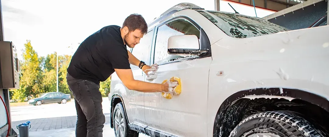 A man is washing a white truck with a sponge at a car wash.
