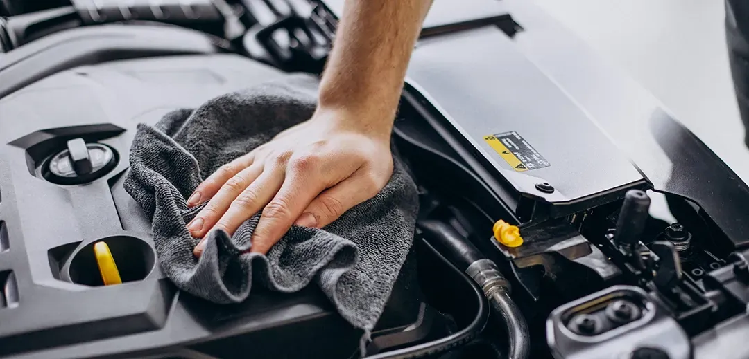 A person is cleaning the engine of a car with a towel.