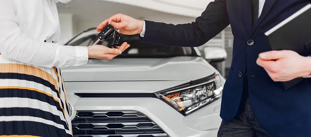 A man is giving a woman a car key in front of a car.