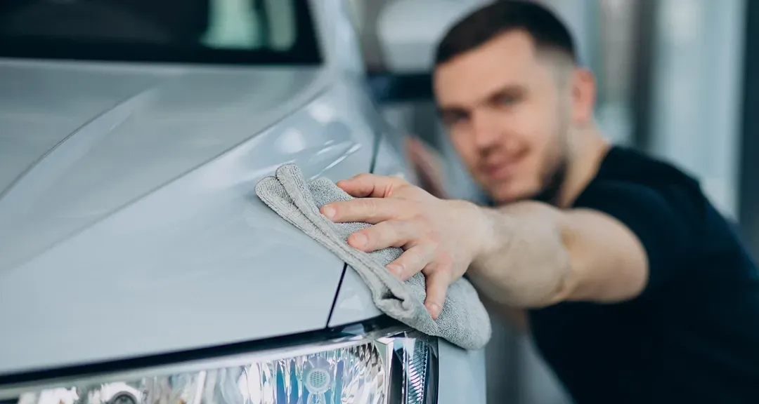 A man is cleaning a car with a towel.
