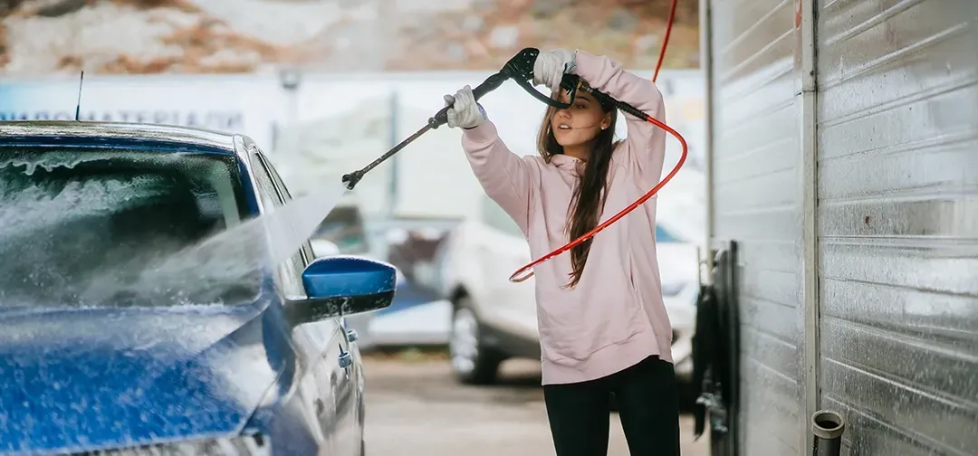 A woman is washing a blue car with a high pressure washer.