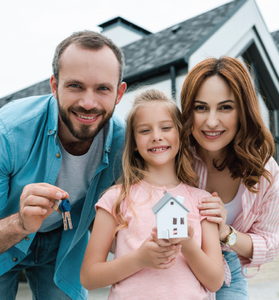 Smiling family holding a small house model in front of a home