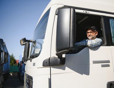 Driver leaning out of a white truck cab, smiling on a sunny street