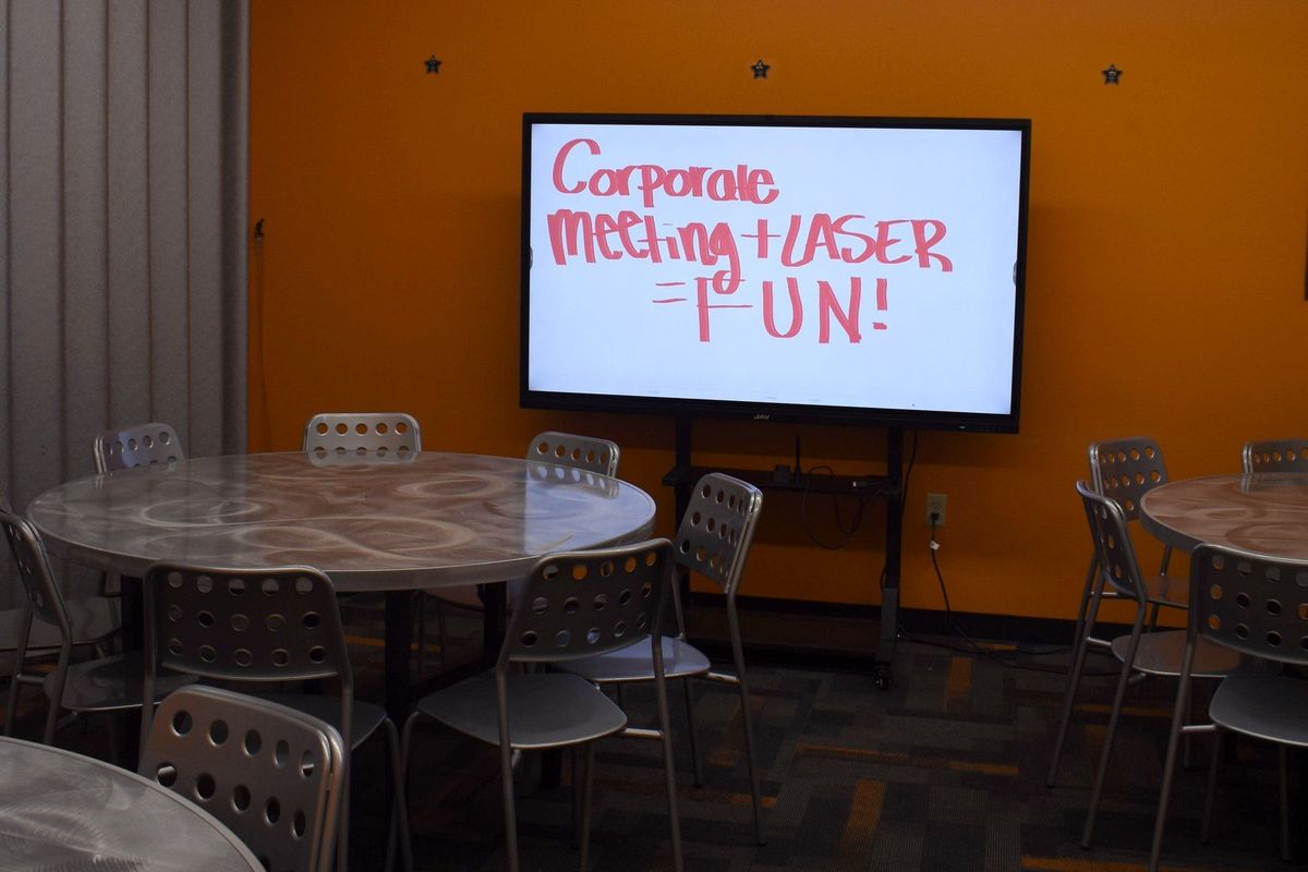 A meeting room at Zone 28 in Pittsburgh set with round tables, the smart board reading Corporate Meeting plus Laser equals Fun