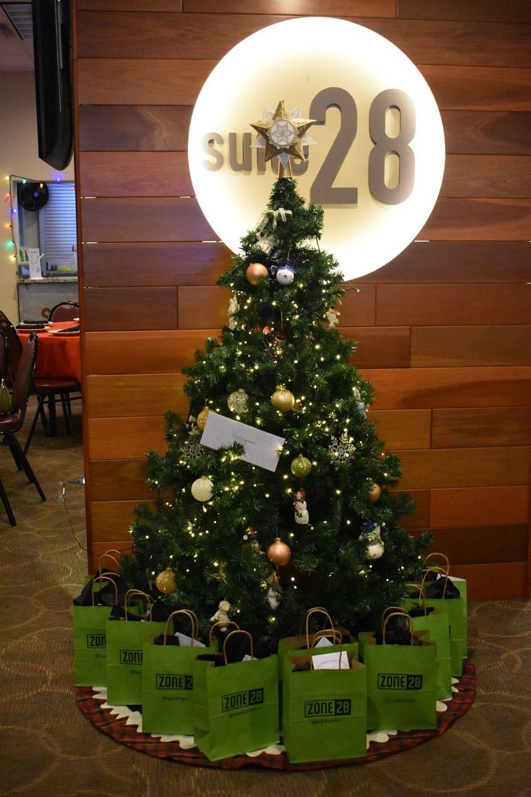 A decorated Christmas tree with green Zone 28 gift bags beside the lit Suite 28 sign at Zone 28 in Pittsburgh
