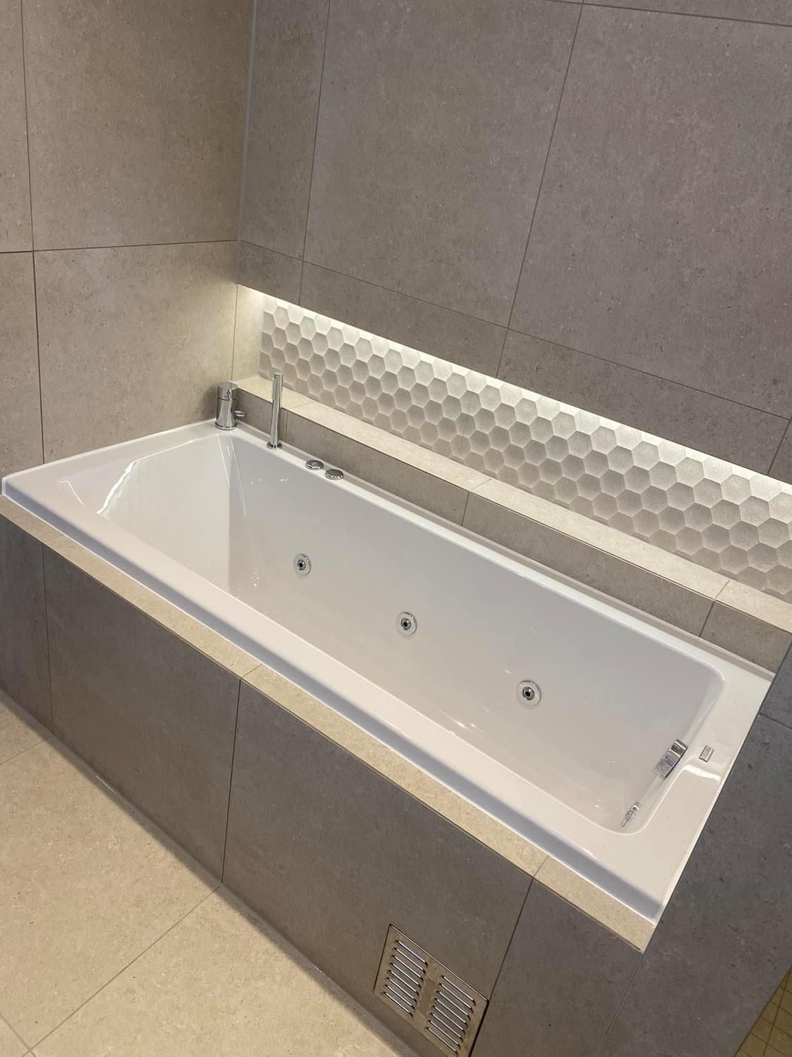 Moderne bad med hvitt boblebad. Grå fliser på veggene og bikakelignende fliser.