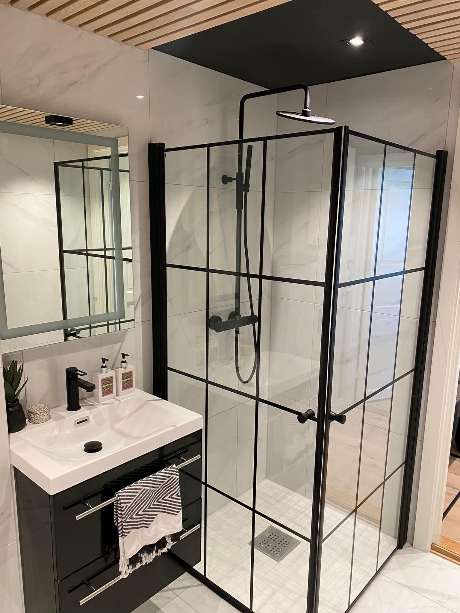 Moderne bad med svart innrammet glassdusj, svart servant og fliser i marmorutseende.