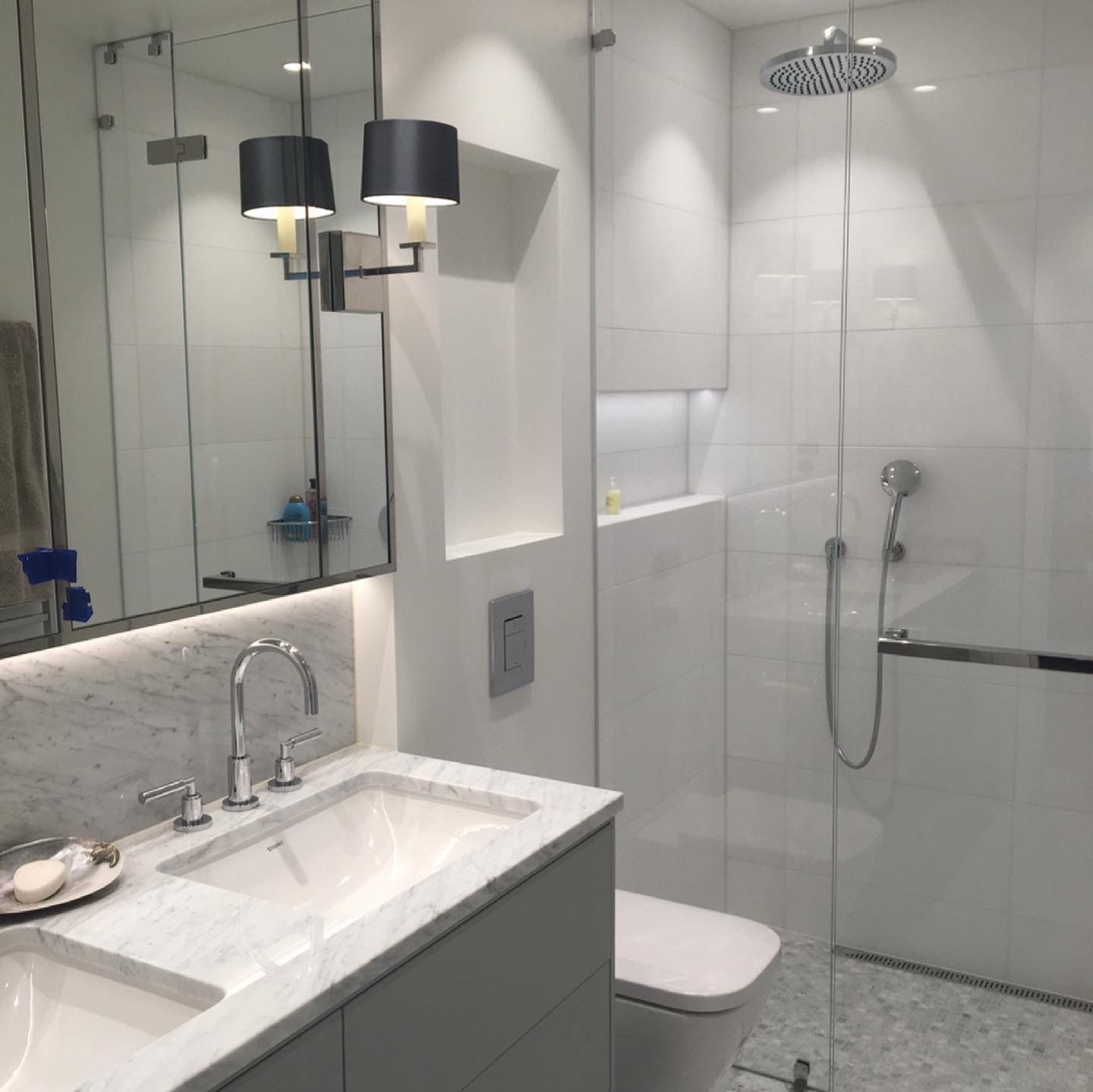 Klassisk moderne hvitt bad med marmorvask, glassvegger og takbelysning.