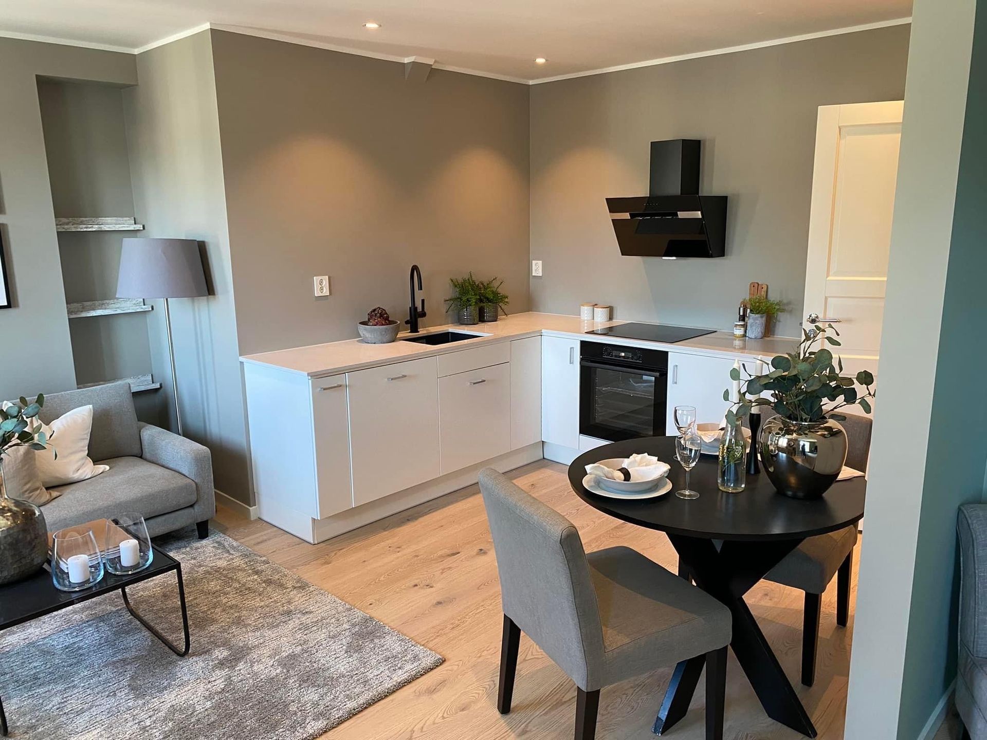 Moderne kjøkken og spisestue med hvite skap, grå vegger og et rundt bord.