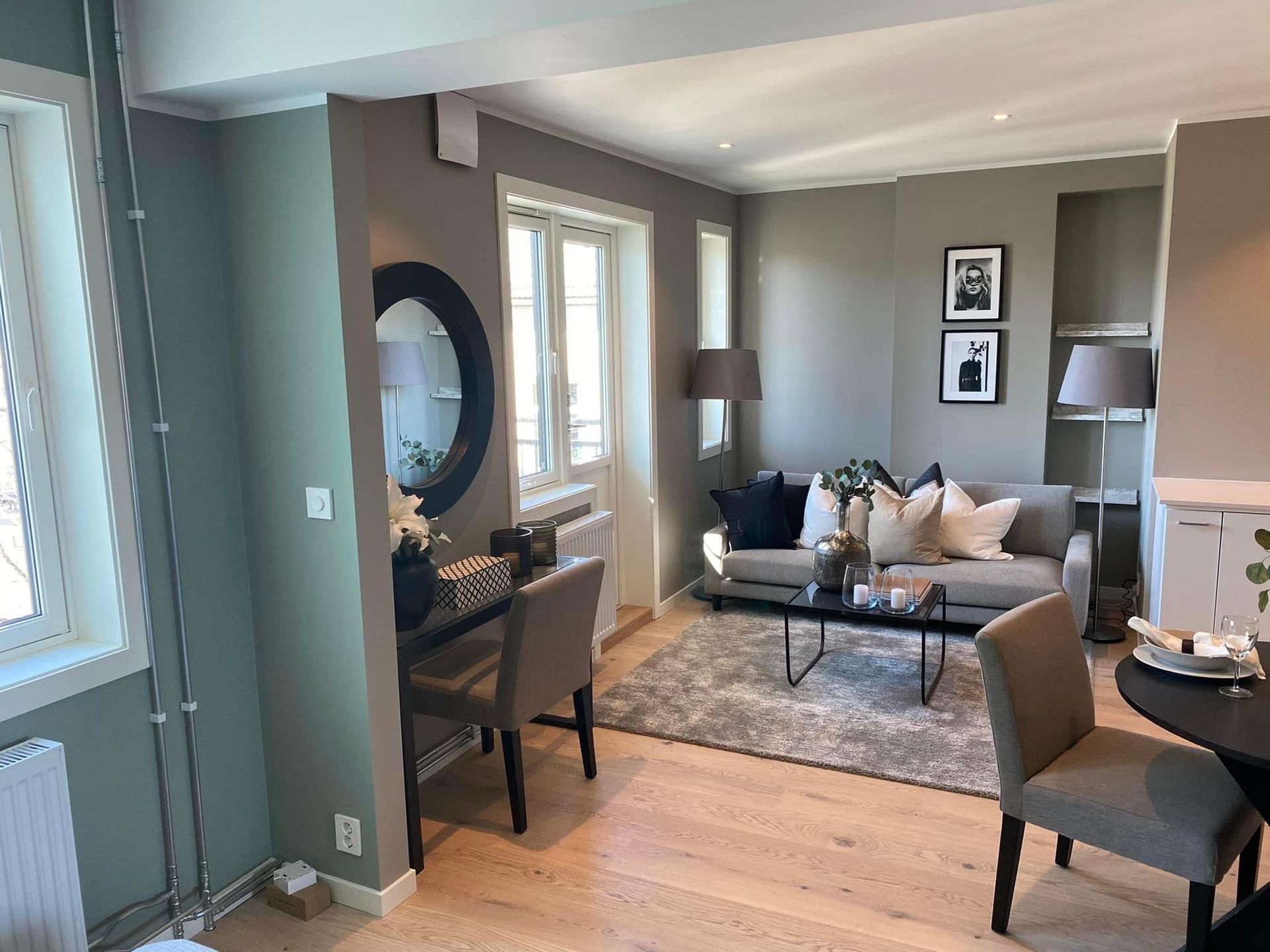 Stue med grå og grønne vegger, sofa, skrivebord og et stort rundt speil.