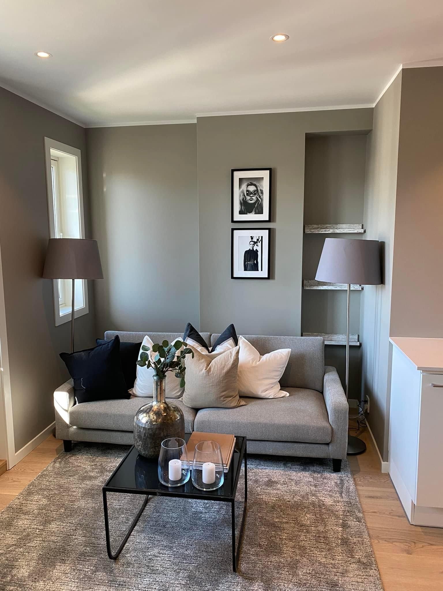 Stue med grå sofa, mønstret teppe, to lamper og innrammet kunst på en gråbeige vegg.