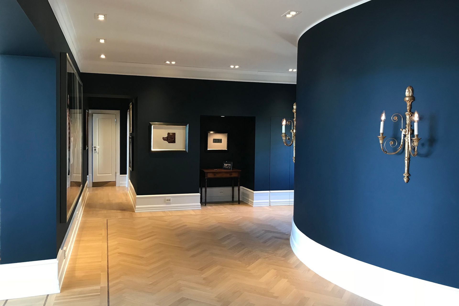 Mørkeblå gang med kunstverk ,fiskebensgulv og utsmykkede lampetter.