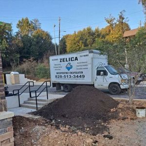 White Zelica moving truck beside a dirt pile and stairs in a residential yard.