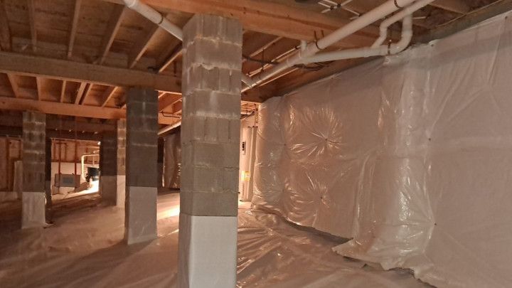 Basement under renovation with plastic sheeting, exposed beams, and wrapped columns