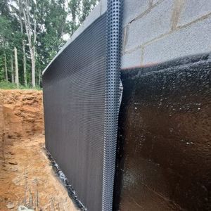 Black waterproofed retaining wall with drainage mesh beside a dirt excavation site