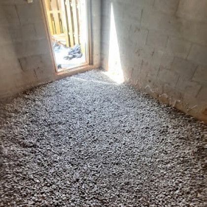 Gravel-covered unfinished room with concrete block walls and a doorway to a bright exterior