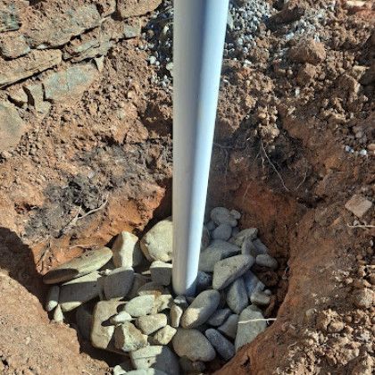 White PVC pipe in a dirt trench surrounded by rocks and gravel.
