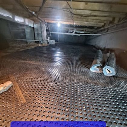Inside a low attic crawlspace, a perforated metal floor and rolled insulation sit under exposed beams.
