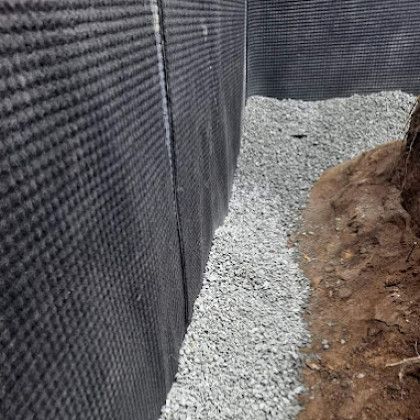 Black landscape fabric edging a gravel trench beside exposed soil and roots