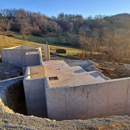 Concrete foundation under construction on a hillside, with rural fields and trees in the background