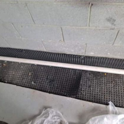 Concrete wall beside a black rubber floor mat and gray floor with a white cable