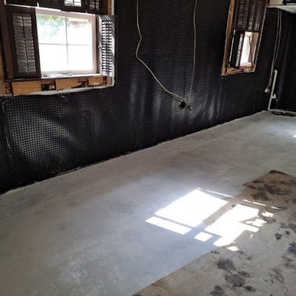 Empty room with unfinished black walls, windows, and a bare concrete floor with sunlight patch.