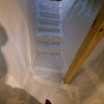 Narrow indoor stairwell painted white with blue steps and a wooden support beam on the right.