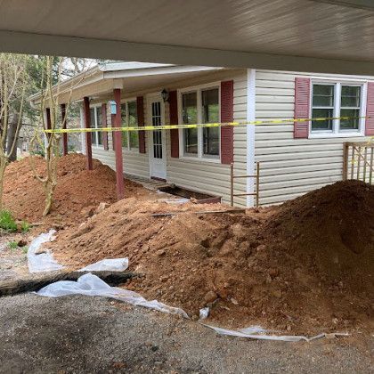 House exterior with large piles of dirt and plastic sheeting along the foundation, suggesting landscaping or drainage work