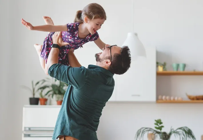 Man lifting a smiling child overhead in a bright kitchen
