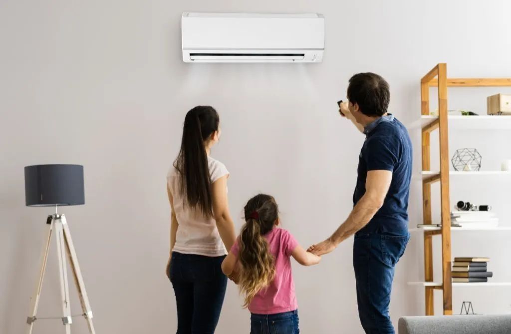 Family standing in a living room, looking at a wall-mounted air conditioner.
