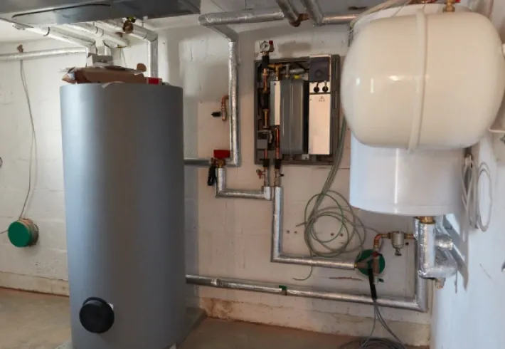 Utility room with a large gray water heater, white expansion tank, and wall-mounted pipes and controls
