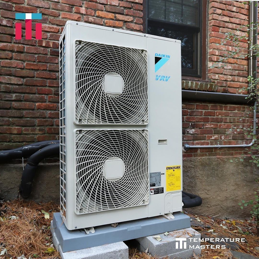 Outdoor white HVAC unit with two large fans mounted against a brick wall.