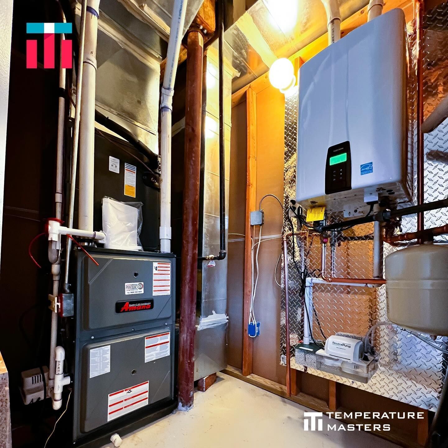 Basement utility room with furnace, water heater, ducts, and a wall-mounted boiler against brick and pipes