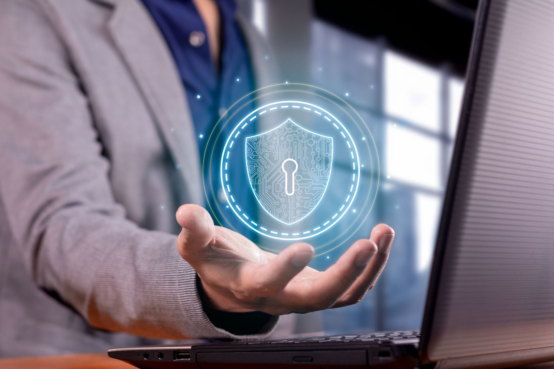 A person is holding a shield with a keyhole in front of a laptop computer.