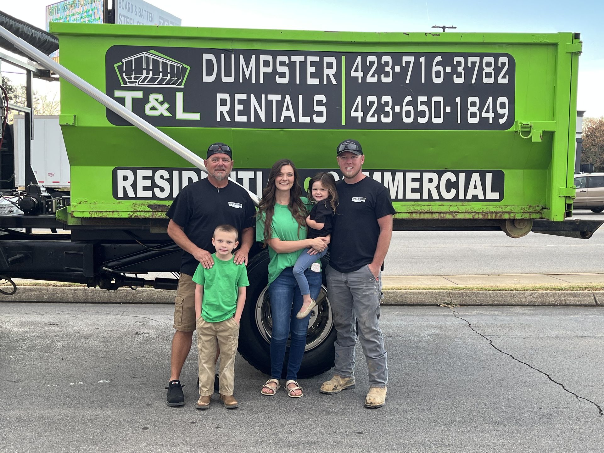A family is posing for a picture in front of a dumpster.