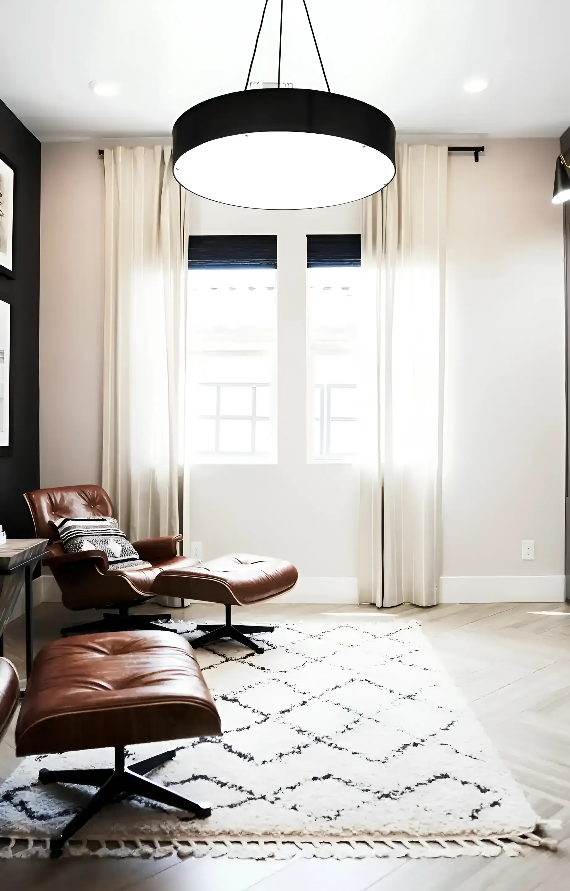 Modern living room with leather lounge chairs, a white rug, and large windows with curtains.