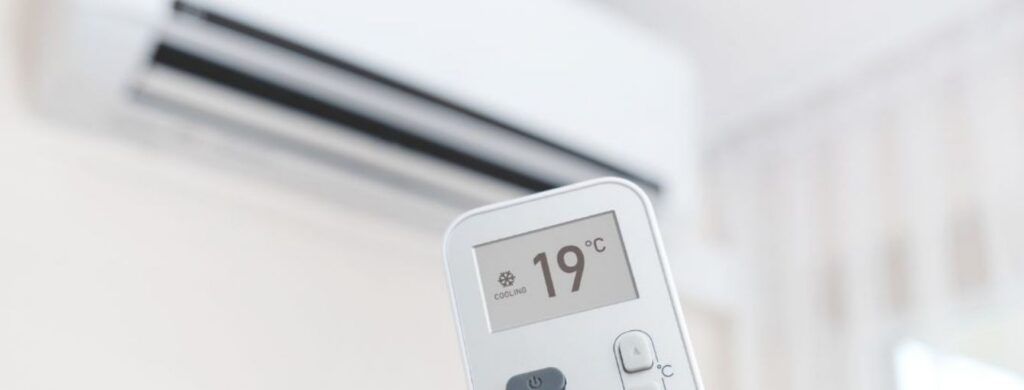 Air conditioner remote showing 19° in front of a wall-mounted AC unit