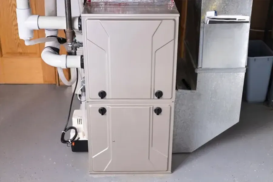 Beige furnace unit in a basement utility room with white pipes and silver ductwork