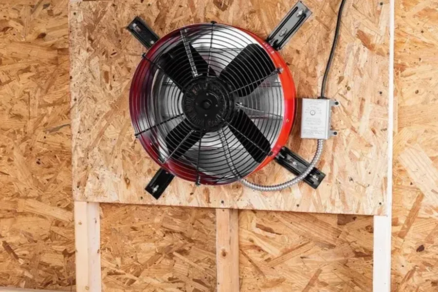 Red-and-black wall-mounted fan installed on plywood inside an unfinished room