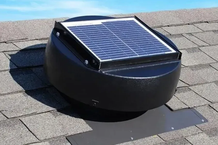 Solar-powered roof vent with black dome and blue panel on gray shingles under a blue sky