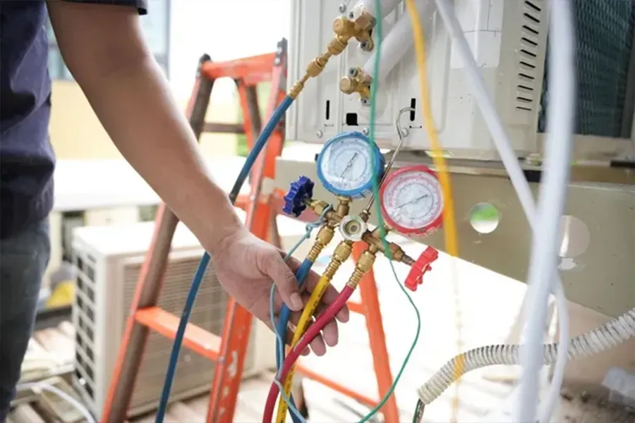 Technician adjusting gauges on a refrigerant manifold next to HVAC equipment and hoses