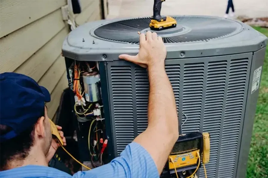Technician repairing an outdoor air conditioner unit with tools beside a house