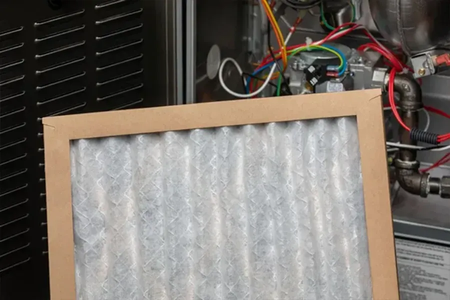 Dirty air filter with cardboard frame beside tangled wires in an appliance interior