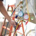 Technician adjusting gauges on industrial HVAC equipment with colored hoses in a workshop