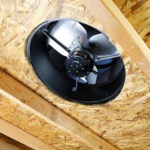 Black ceiling-mounted exhaust fan in a wood-framed attic vent opening