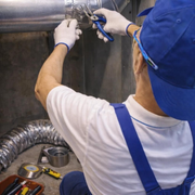 Mechanic repairing pipes under a sink with tools and gloves