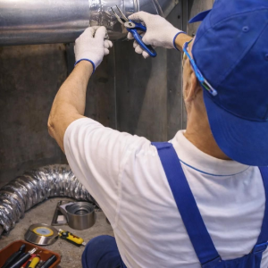 Worker in blue vest welding silver HVAC ducts in an industrial setting