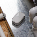 Small gray device on a metal surface between white pipes in a utility space